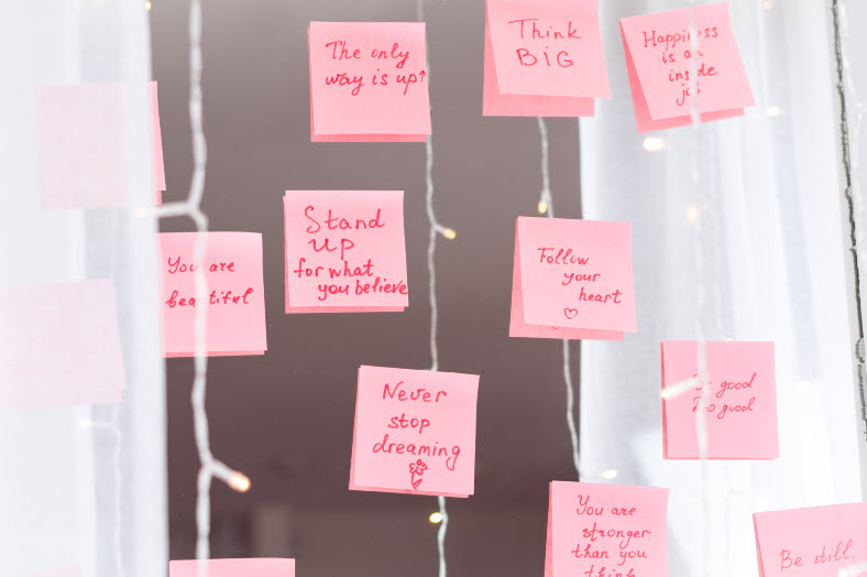A window decorated with pink sticky notes containing inspirational messages such as 'The only way is up,' 'Think BIG,' 'Happiness is inside you,' and 'Never stop dreaming.
