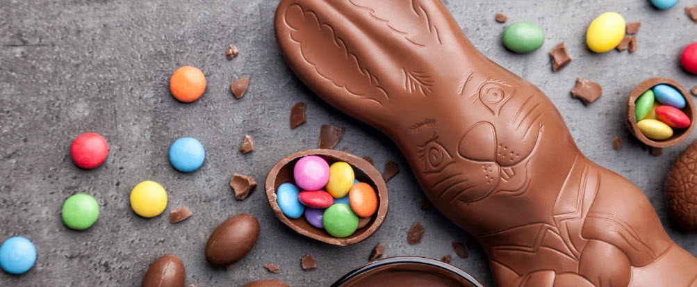 A chocolate Easter bunny surrounded by brightly colored candy, illustrating the commercialization of Easter, overshadowing its spiritual significance of rebirth and renewal.