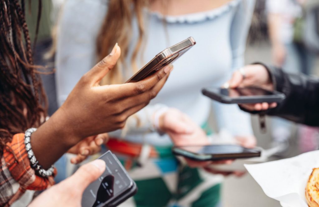 A scene where a group of high-school students are holding on to their digital device. It's about how devices are inseparable from kids today making it harder for parents teaching children.