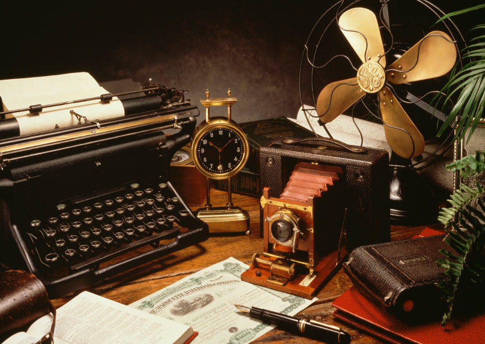 Antique typewriter, clock, camera, and fan sits atop a wooden desk. A book is open, a pen lay across a stock certificate. We are not trapped in a cycle of unfulfillment. Break free from the herd.