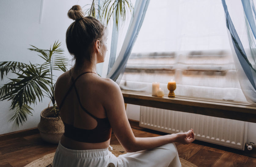 A woman poised in a mediation mode having a deeper connection by bringing calmness into her day. In the platform before her are lit candles for the ambience of spiritual connection.