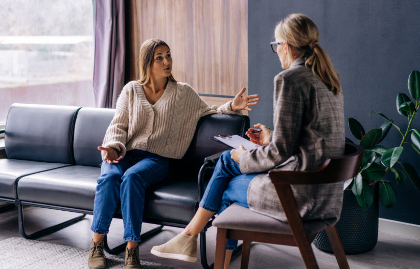 A woman dressed in jeans and a sweater talking with a psychiatrist about feelings of disconnection from her burnout in life.