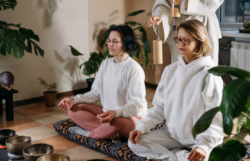 Two women sitting in a meditative position with a sound practitioner. It embodies mindfulness in healing mind, body and soul.