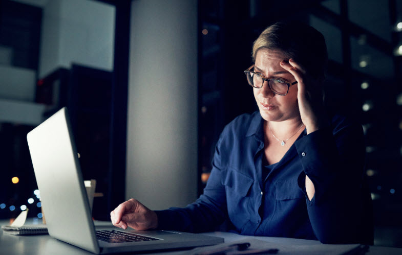 A woman is looking at her computer screen. It appears to be night and she appears tired. It depicts how virtue is not performance but rather a practice.