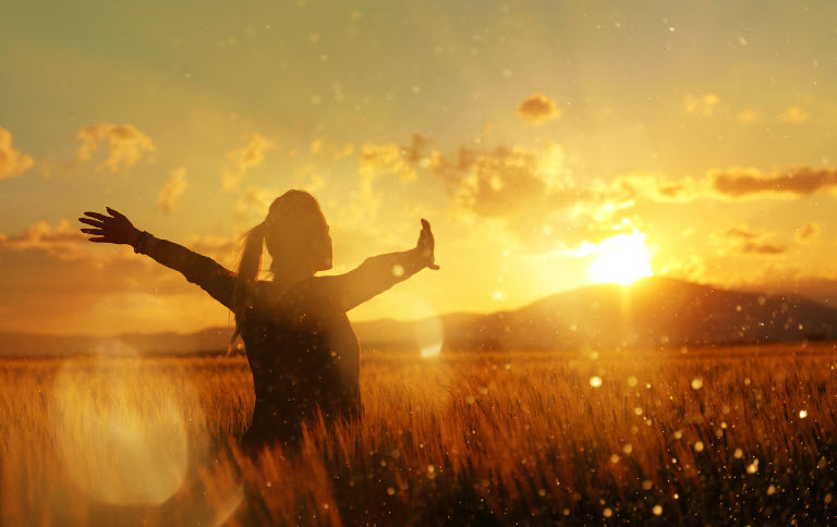 A woman with outstretched arms, stands in a field of wheat. The sun radiates its golden rays of light as it sinks behind a mountain top. It depicts how you are not powerless in this story. You are the pulse. The compass. The call.
