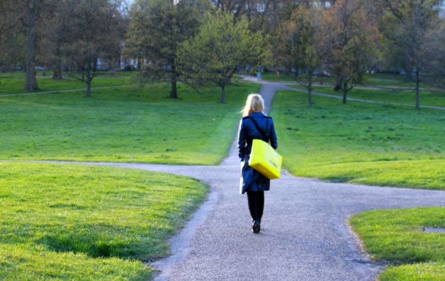 A woman in a black coat and yellow shopping bag stands at a crossroads on a quiet pathway, contemplating her next step.
This conveys her moment of decision-making, capturing the uncertainty and possibility of new directions.